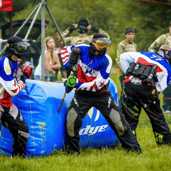 Dvě osoby hrají paintball a skrývají se za překážkami.
